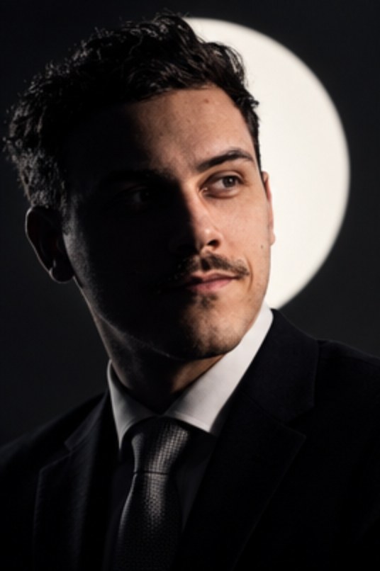 Portrait of Maxime Najmaoui in a dark suit, half in shadow